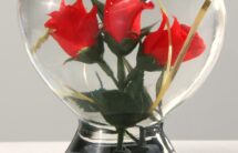 Fotografia szklanego serca z 3 sztucznymi czerwonymi różami w środku.