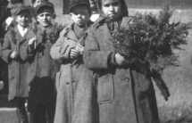 Czarno-biała fotografia - grupa dzieci w ciepłych płaszczach, z palmami w ręku, w tle mur kościoła.