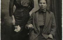 Czarno-biała fotografia: starsza kobieta siedzi, młodsza stoi obok.