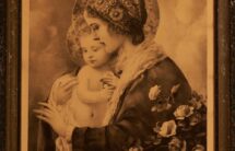 Obraz w kolorach sepii: młoda kobieta z profilu, w haftowanym czepku, z dzieckiem na ręku. Na dole napis „Matka Boska Błogosławiąca”.