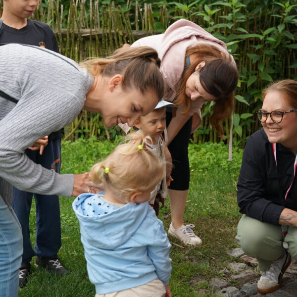 Dwie kobiety pochylają sie nad dziećmi, trzecia kobieta kuca, uśmiecha się 