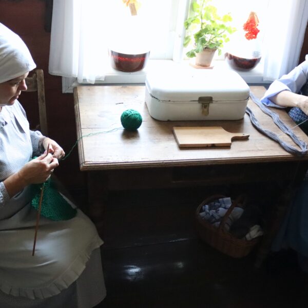 Dwie kobiety w olenderskich strojach siedzą przy stole kuchennym i robią na drutach