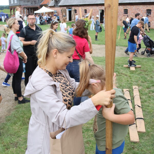 Kobieta pomaga dziewczynce wejśc na drewniane szczudła 