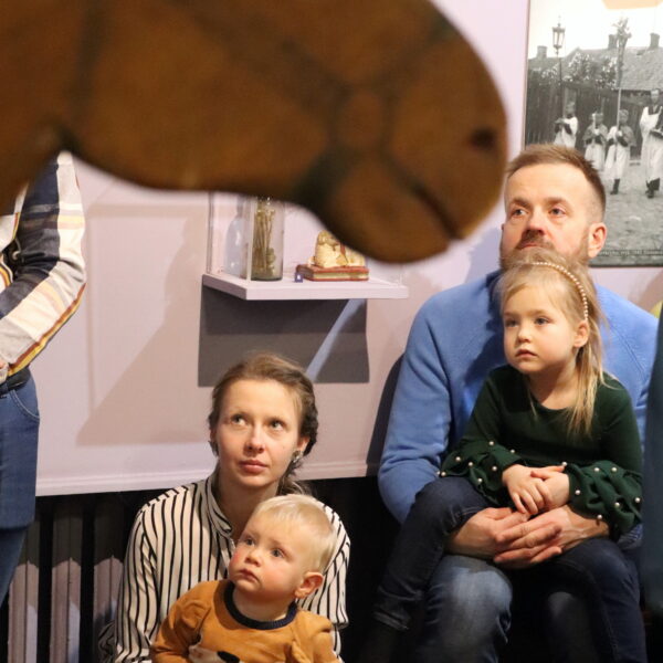 Rodziny z małymi dziećmi zebrane w sali muzeum, na pierwszym planie drewniana głowa konia 