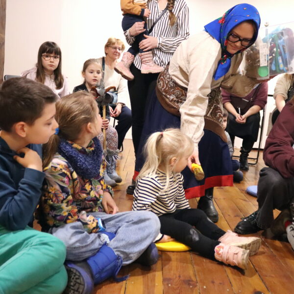 Rodziny z małymi dziećmi zebrane w sali muzeum. 