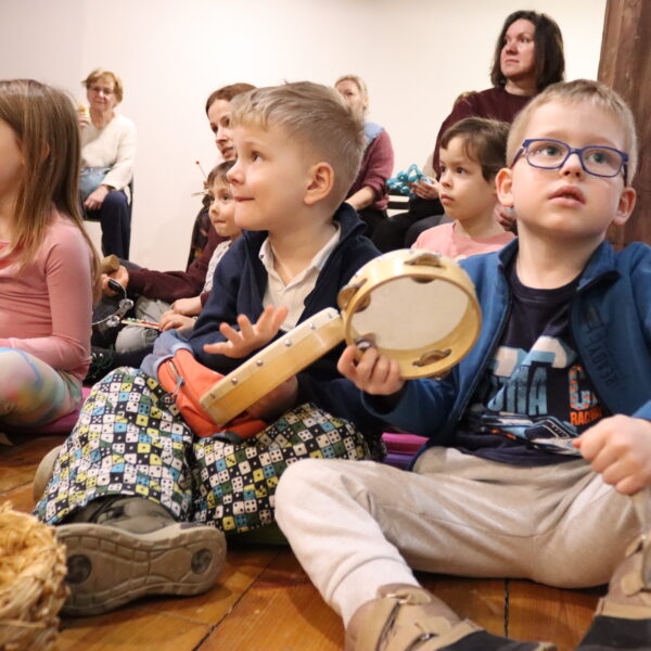 Rodziny z małymi dziećmi zebrane w sali muzeum. W rękach instrumenty. 