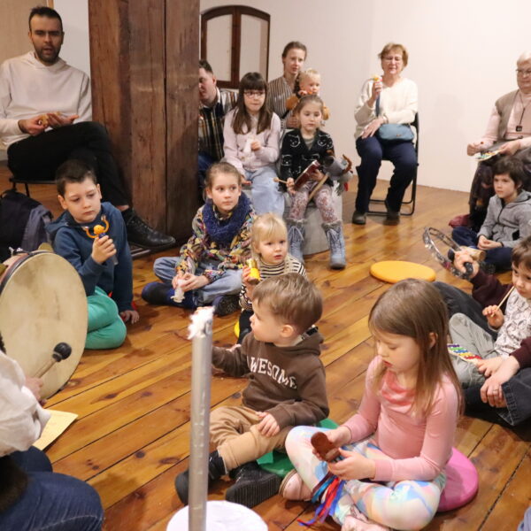 Rodziny z małymi dziećmi zebrane w sali muzeum. 