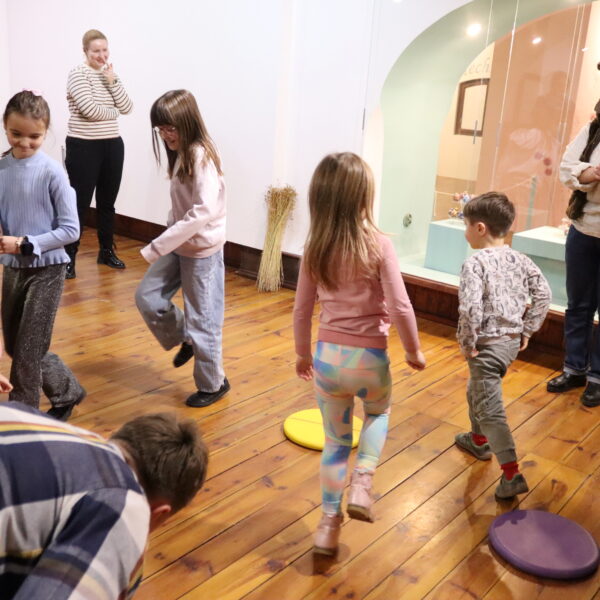 Dzieci skaczą i biegają między kolorowymi okrągłymi poduszkami w sali 