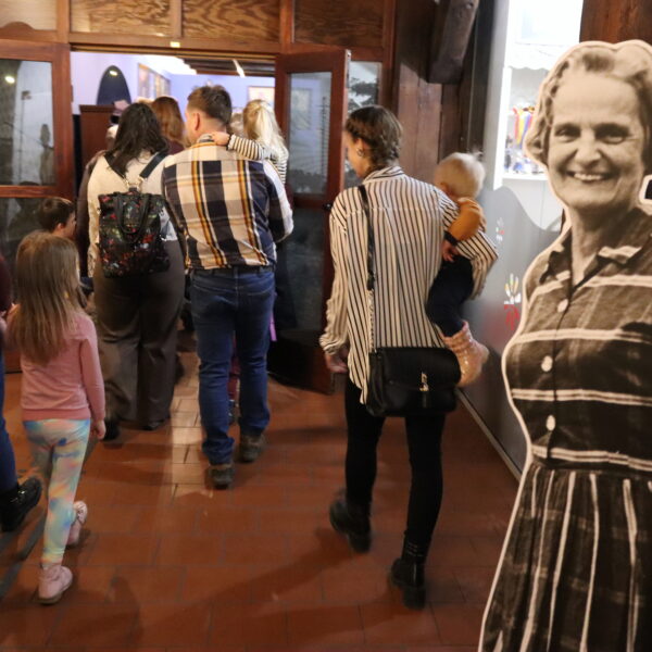 Po prawej czarno-biały stand z postacią kobiecą. W tle ludzie wychodzący z budynku. 
