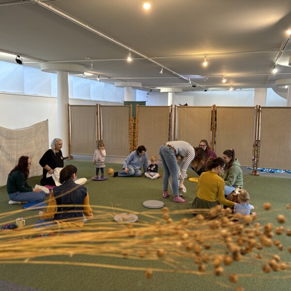 Kobiety z dziećmi bawią się w sali na zielonej wykładzinie,na pierwszym planie bukiet lnu 