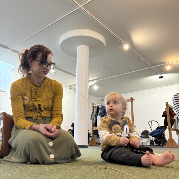 Kobieta siedzi na zielonej wykładzinie, obok małe dziecko z bosymi stopami. 