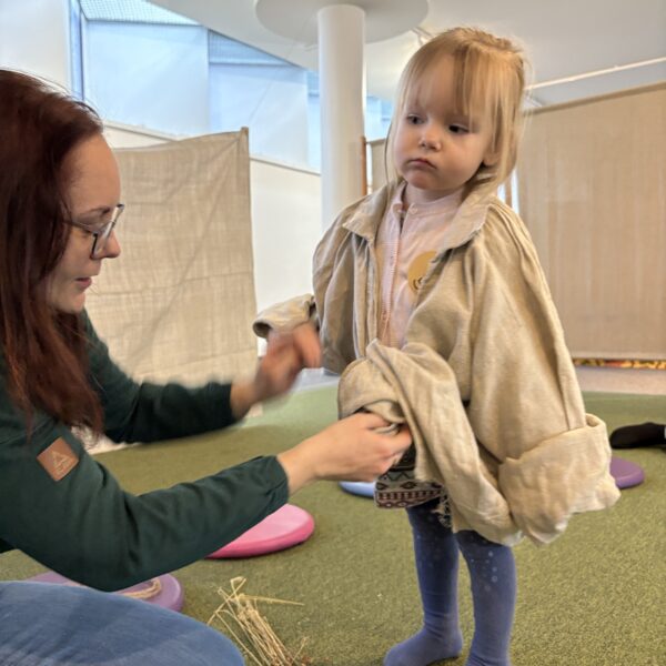 Kobieta nakłada na dziewczynkę lnianą koszulę. 