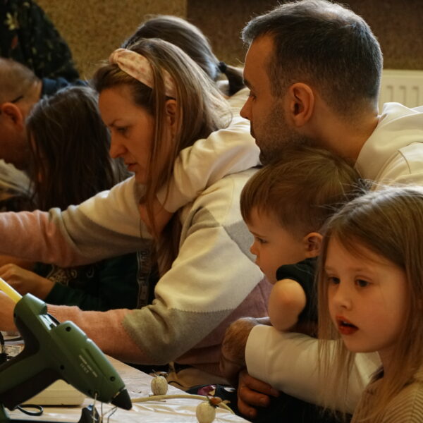 Siedzący przy tole ludzie przygotowują ozdoby wielkanocne. 