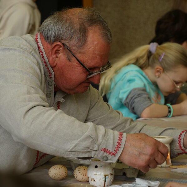 Mężczyzna w stroju kurpiowkim zdobi jajko woskiem pszczelim 