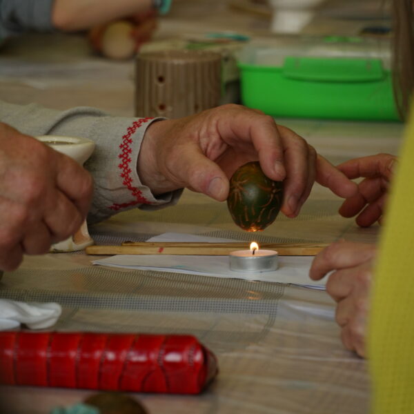 Męska dłoń trzyma ozdobione jajko nad podgrzewaczem 