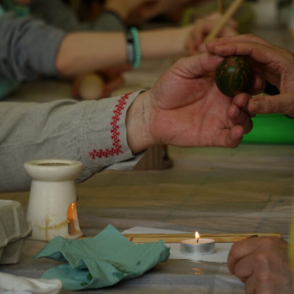 Męska dłoń podaje ozdobione jajko. 