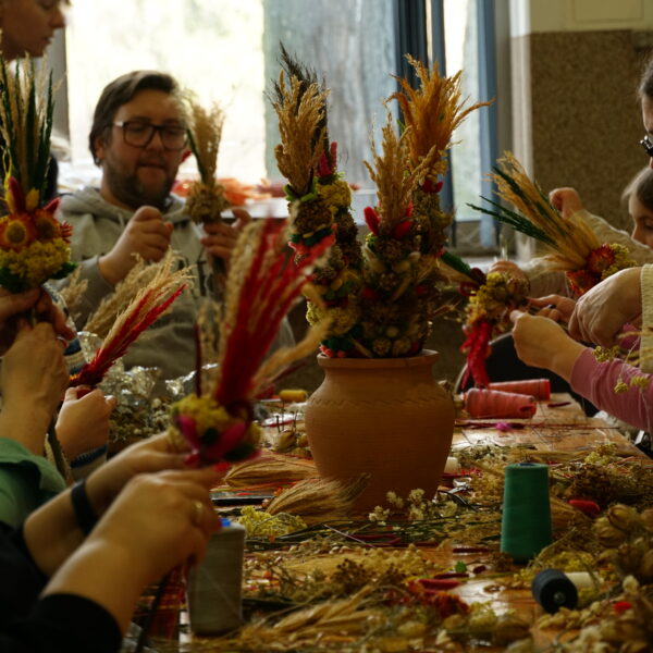 Zebrani przy stole ludzie przygotowują palmy wielkanocne. 