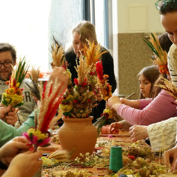 Zebrani przy stole ludzie przygotowują palmy wielkanocne. 