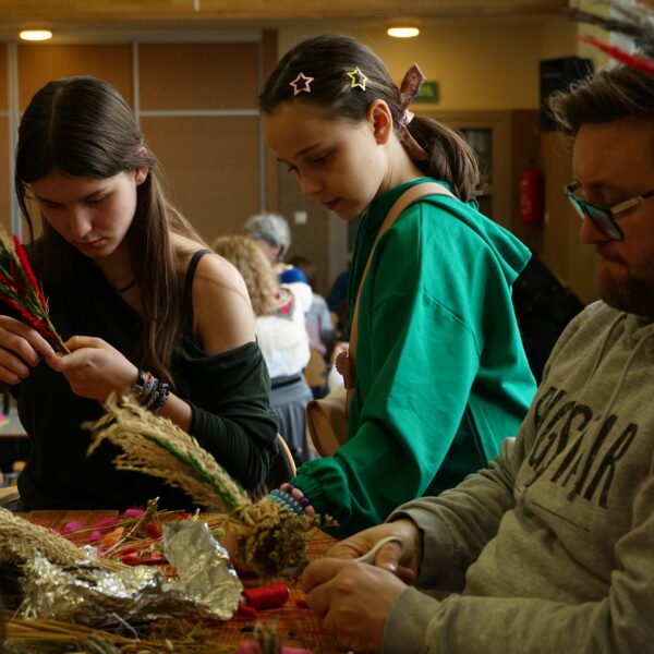 Mężczyzna i dwie dziewczynki przygotowują palmy wielkanocne. 