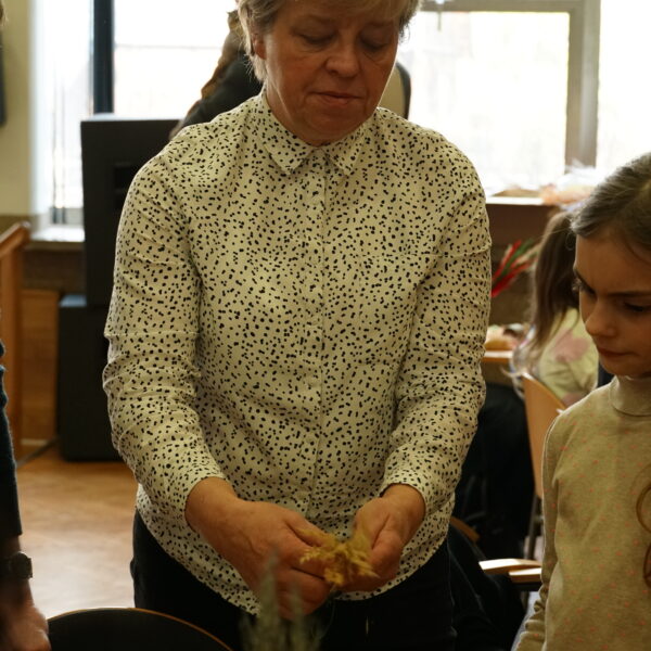 Kobieta demonstruje dziewczynce, jak wykonać wielkanocną palmę - w rękach trzymają gałązki. 