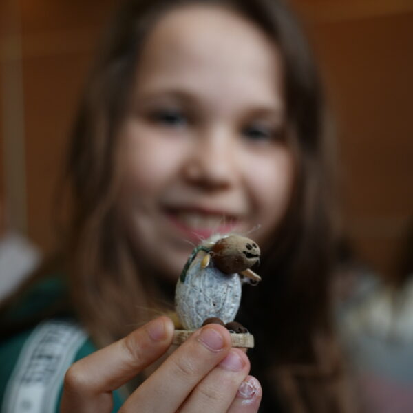 Dziewczynka trzyma baranka wykonanego z orzechów i ziarnek. 