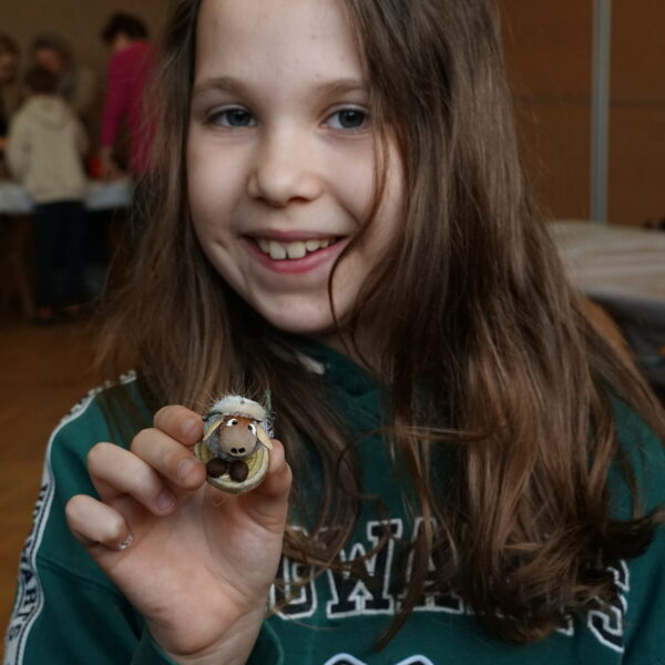 Dziewczynka trzyma baranka wykonanego z orzechów i ziarnek. 