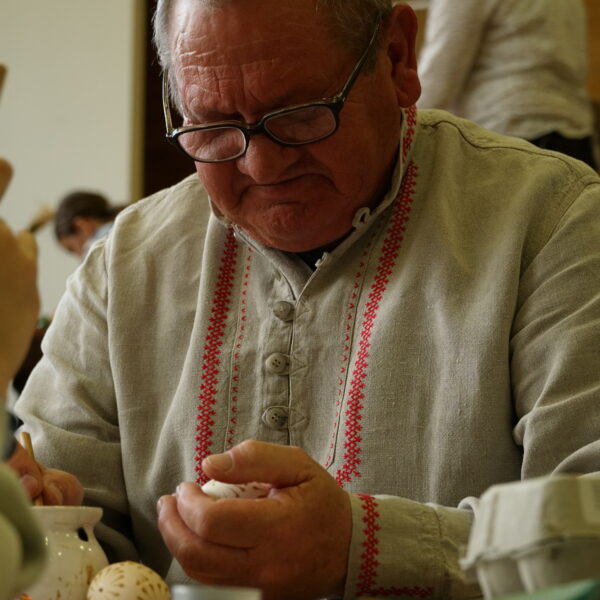 Mężczyzna w stroju kurpiowkim zdobi jajko woskiem pszczelim 