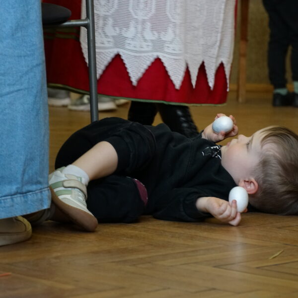 Mały chłopiec trzymający w dłoniach styropianowe jajka leży na podłodze 