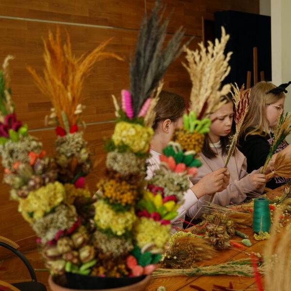 Zebrani przy stole ludzie przygotowują palmy wielkanocne. 