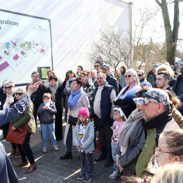 Grupa ludzi słucha przewodnika w parku etnograficznym. 