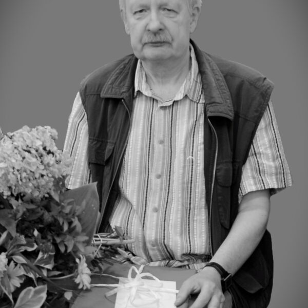 Mężczyzna siedzi na krzesle z prezentem w ręce, obok kwiaty