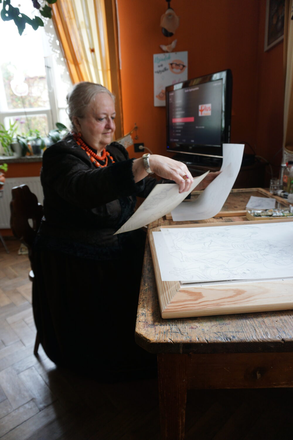 Starsza kobieta siedzi przy biurku z dokumentami.