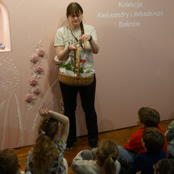 Siedzące na podłodze dzieci wpatrują się w kobietę.