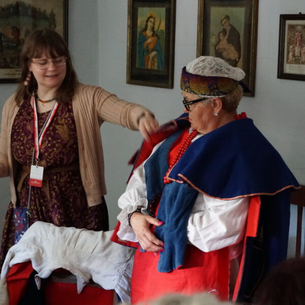 Kobieta przymierza strój kujawski - pomaga jej pracownica muzeum