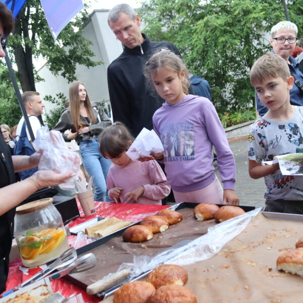 Kobieta na stoisku gastronomicznym pakuje bułeczki, dzieci obserwują 