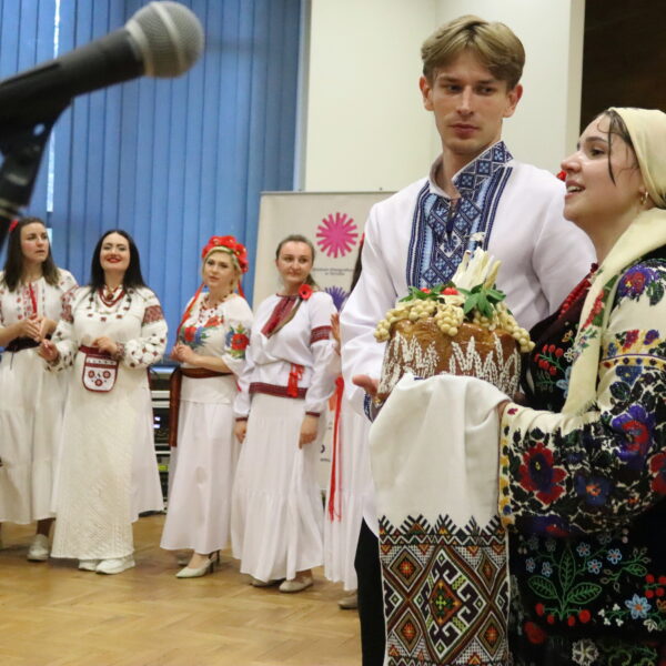 Ludzie w tradycyjnych strojach ukraińskich, na pierwszym tle para przy mikrofonie 