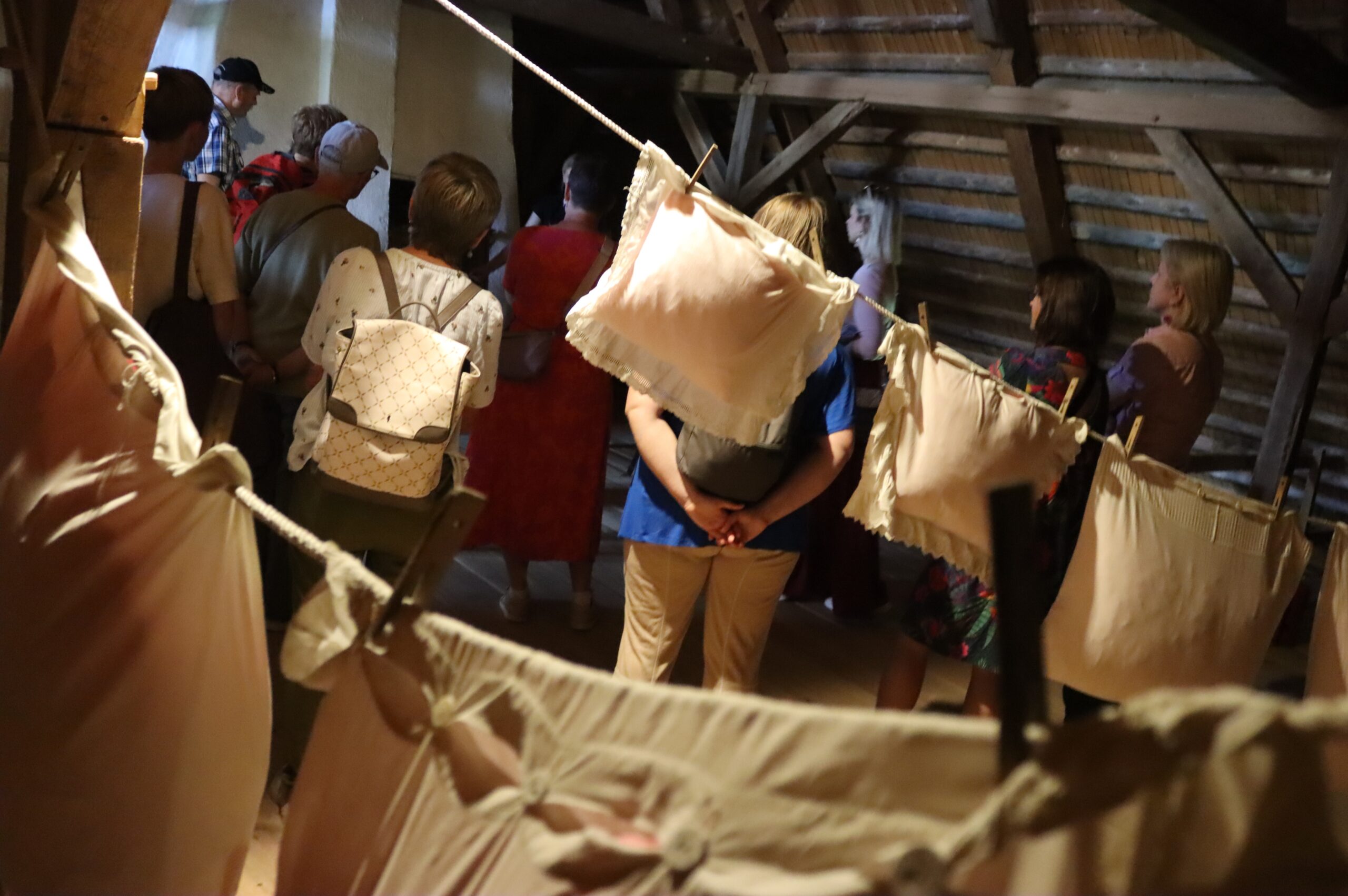 Poduszki i bielizna zawieszone na lince na praniew, w tle ludzi zwiedzający chałupę